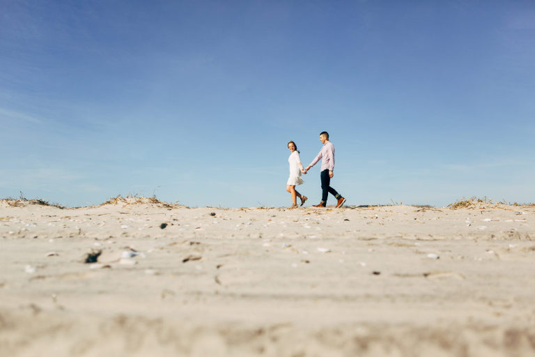 Engaged couple walk on beach in Ocean City winter engagement session. 