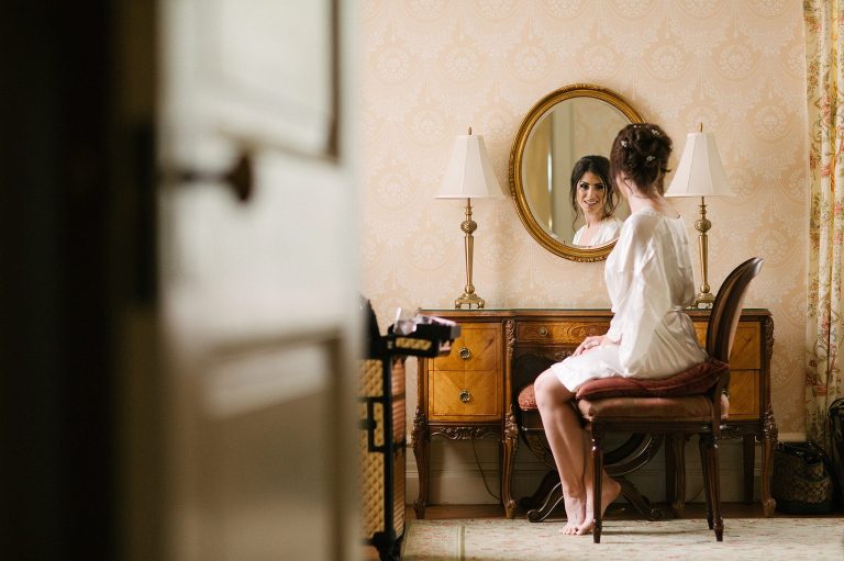 Bride looks into mirror as she gets ready for her wedding at Cairnwood Estate