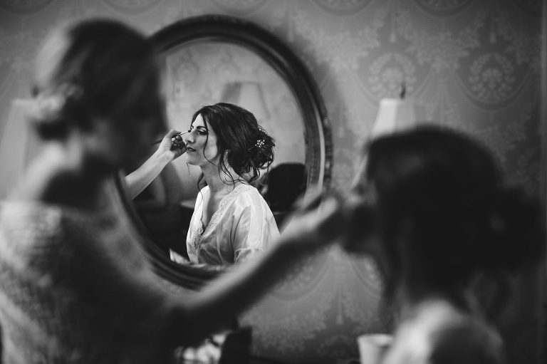 Black and white image of bride having make up done at Cairnwood Estate in Bryn Athyn, PA.